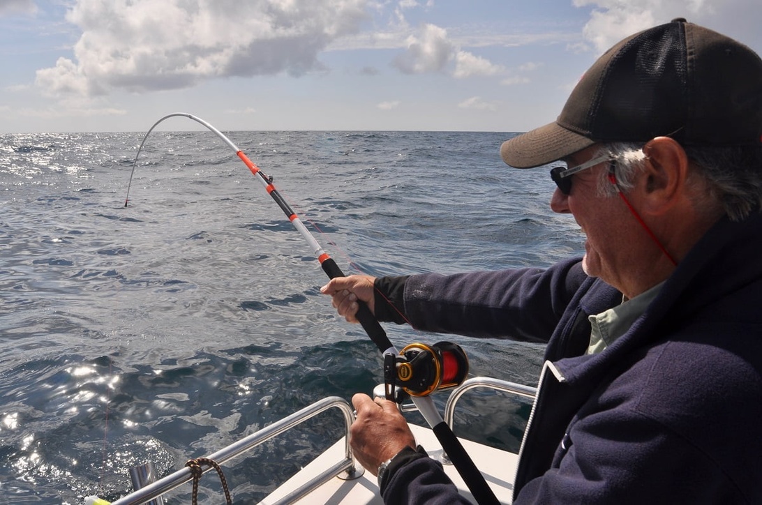 En fiskare i en båt på havet, med böjt spö som indikerar ett napp.